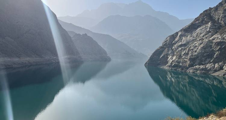 Ruhiger Bergsee mit steilen Felshängen, die sich in kristallklarem türkisfarbenem Wasser unter diffusem Morgenlicht spiegeln.