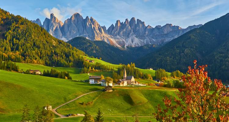 Idyllisches Alpental mit üppigen grünen Wiesen, die zu den dramatischen Dolomitengipfeln bei Sonnenaufgang führen.