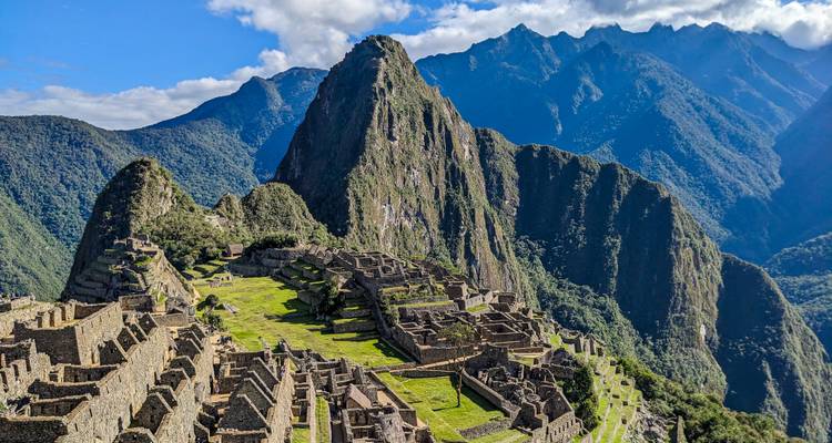 Ikonischer Blick auf die Ruinen von Machu Picchu, eingebettet zwischen steilen Andengipfeln unter blauem Himmel.