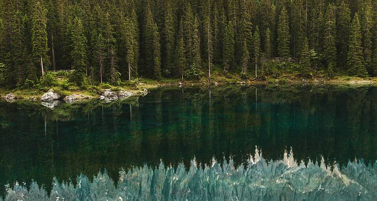 Spiegelstil smaragdgroen meer dat dicht naaldbos en bergtoppen weerkaatst.