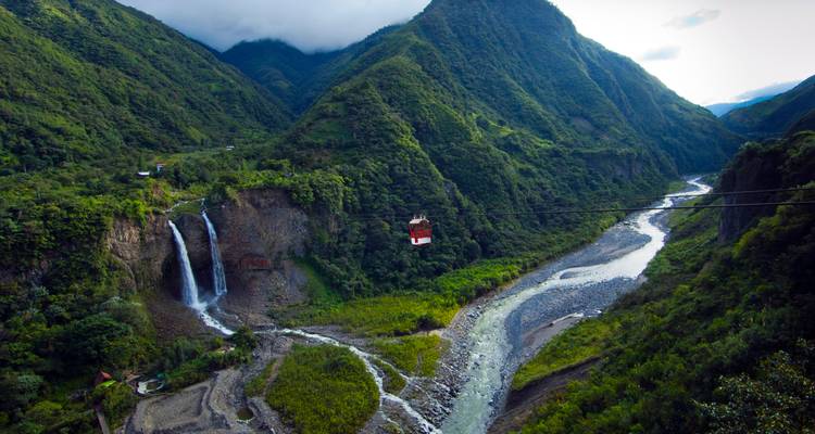 Rote Seilbahn gleitet über ein tiefgrünes Tal mit einem hohen Wasserfall, der neben einem gewundenen Fluss hinabstürzt.