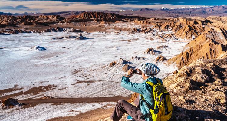 Reisender sitzt am Klippenrand und fotografiert eine weite, unwirkliche Wüstensalzlandschaft.