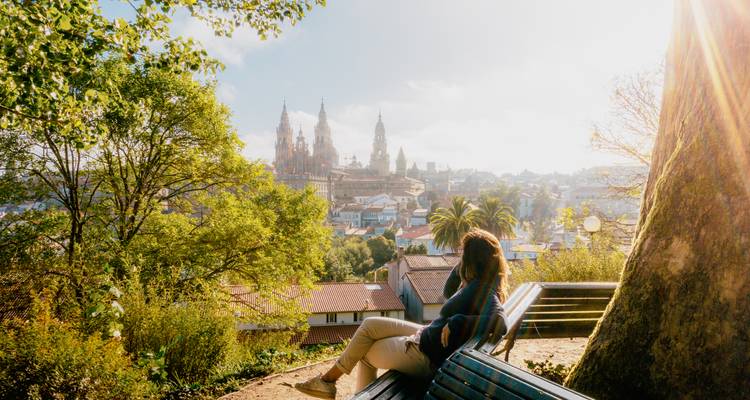 Frau sitzt auf einer Bank mit Blick auf Santiago de Compostela.