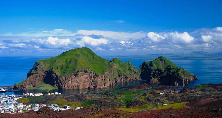 Vue d'une île rocheuse verte entourée par l'océan sous un ciel dégagé.