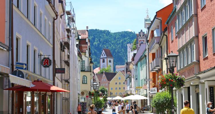 Calle bulliciosa en un pueblo encantador con edificios históricos y vista a la montaña.