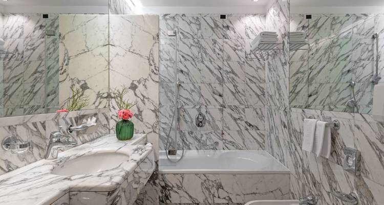 Salle de bain en marbre avec une baignoire, un lavabo et des murs miroirs. Fleurs décoratives sur le comptoir.