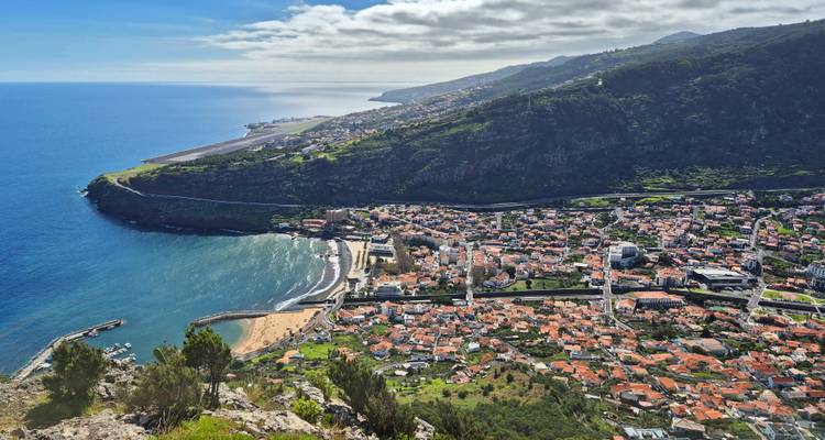 Vue aérienne d'une ville côtière nichée entre l'océan et des falaises luxuriantes.