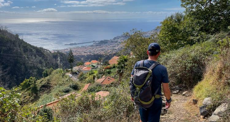 Un homme faisant de la randonnée sur un sentier avec vue sur l'océan et la ville.