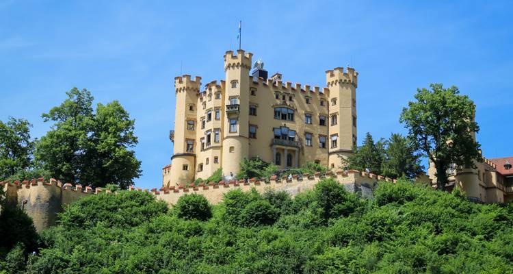 Un château jaune entouré d'une végétation luxuriante sous un ciel bleu clair.