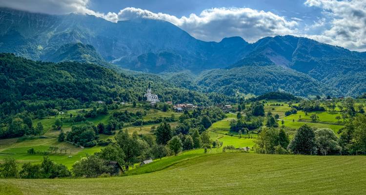 Weites grünes Tal mit verstreuten Häusern und einer Kulisse aus hoch aufragenden Bergen.