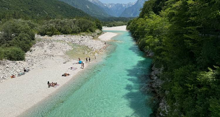 Ein klarer Fluss mit Menschen, die sich an einem sonnigen Tag entspannen, umgeben von üppigem Grün.