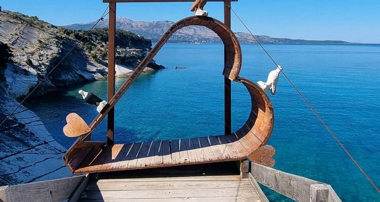 Decoración de madera en forma de corazón con vista a un mar azul claro y una costa rocosa.
