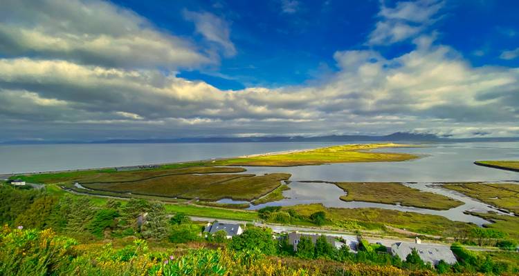 Vivid aerial view of estuary wetlands beneath a dramatic sky with streaks of sunlight