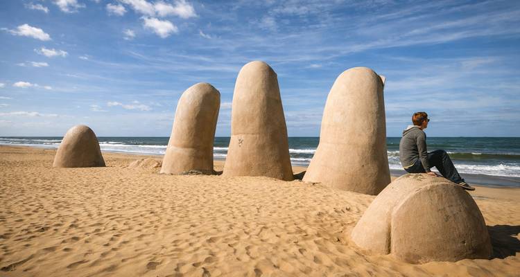 Personne assise sur l'un des doigts sculpturaux sur une plage de sable.