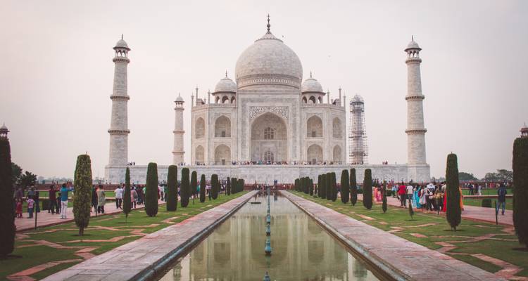 Icónico Taj Mahal de mármol blanco reflejado en su larga piscina reflectante con visitantes a lo largo de los senderos.