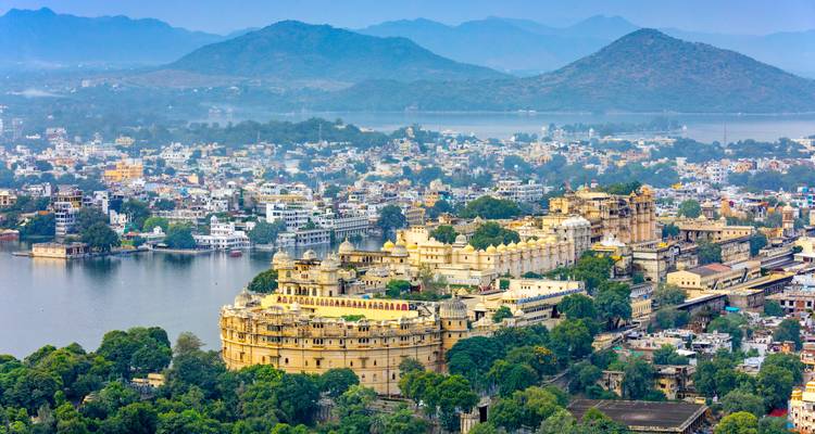 Vista aérea panorámica del complejo del palacio blanco de la ciudad de Udaipur en la orilla de un lago rodeado de montañas.