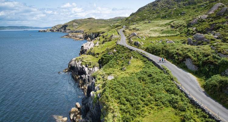 Two walkers enjoy a narrow coastal road hugging dramatic cliffs above the Atlantic