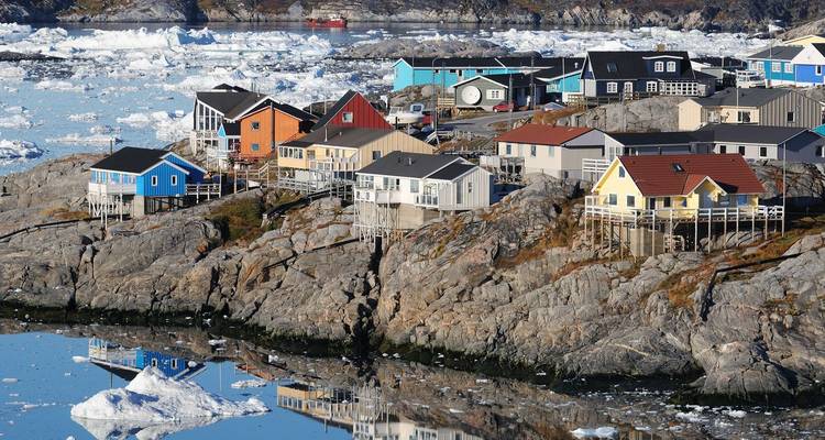 Des maisons colorées sur pilotis s'accrochent à la côte rocheuse bordée d'eaux parsemées d'icebergs au Groenland.