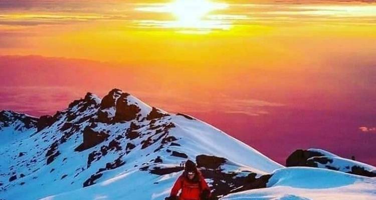 Un alpinista sube por una cresta nevada bañada en la vivida luz anaranjada y rosada del amanecer.