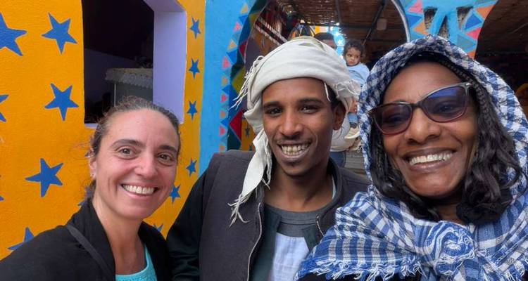 Tres personas sonriendo frente a edificios coloridos.