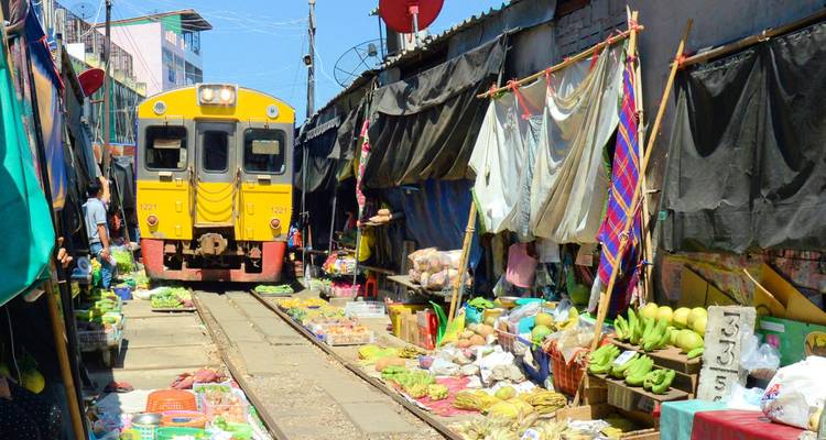 Bright yellow train inches through a bustling street market lined with produce stalls.
