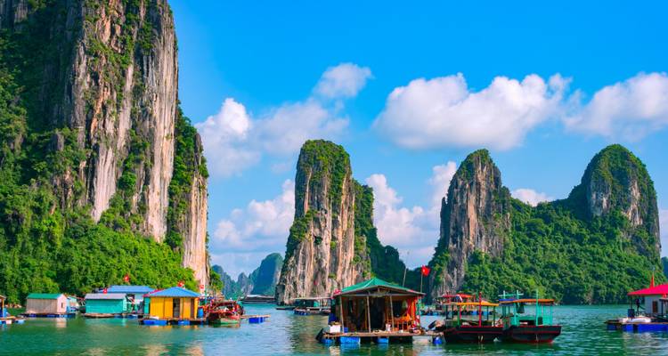 Towering limestone karsts rise from turquoise waters dotted with colorful floating houses and boats.