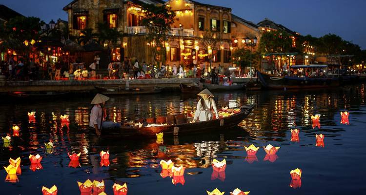 Traditional lantern-lit boat glides along Hoi An’s river at night surrounded by floating candles.
