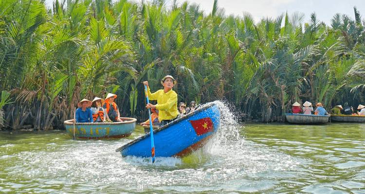 Tourists spin a round basket boat splashing water in a palm-lined canal near Hoi An.