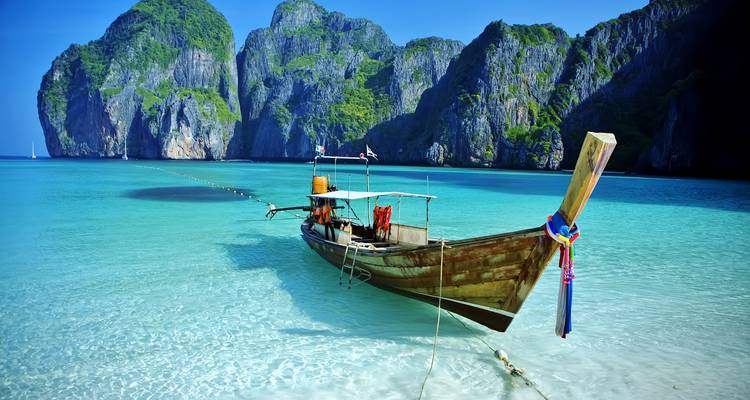 Long-tail wooden boat floating on crystal-clear turquoise water with dramatic limestone cliffs behind.