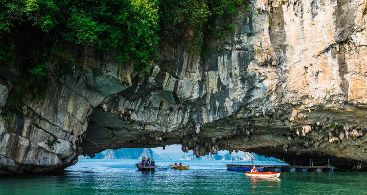 Kayakers paddle beneath a dramatic limestone arch in the emerald waters of Ha Long Bay.