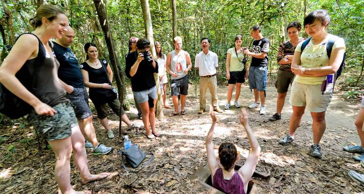 Le groupe de touristes se rassemble tandis qu'un guide démontre comment entrer dans les tunnels de Cu Chi dans la forêt dense.