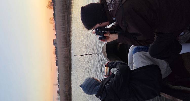 Dos personas sentadas en un barco tomando fotografías durante el atardecer.