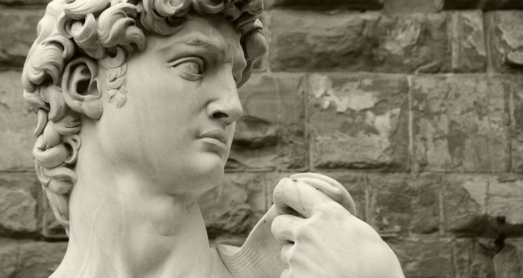 Close-up of a marble statue's face against a stone wall, likely from Florence.