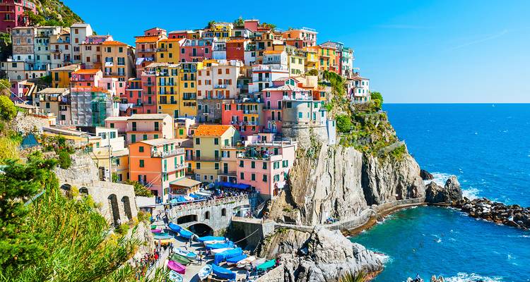 Colorful buildings on a rocky coastline in Cinque Terre under a blue sky.