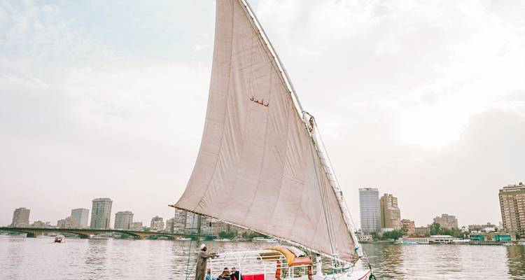 Velero tradicional en un río con un paisaje urbano de fondo.