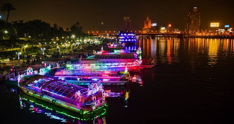 Barcos con luces decorativas en un río por la noche.