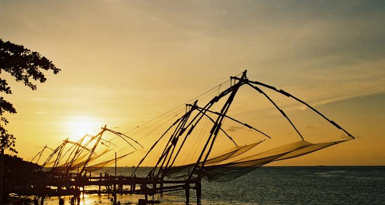Silhouettes de filets de pêche chinois contre un coucher de soleil chaleureux sur l'océan.