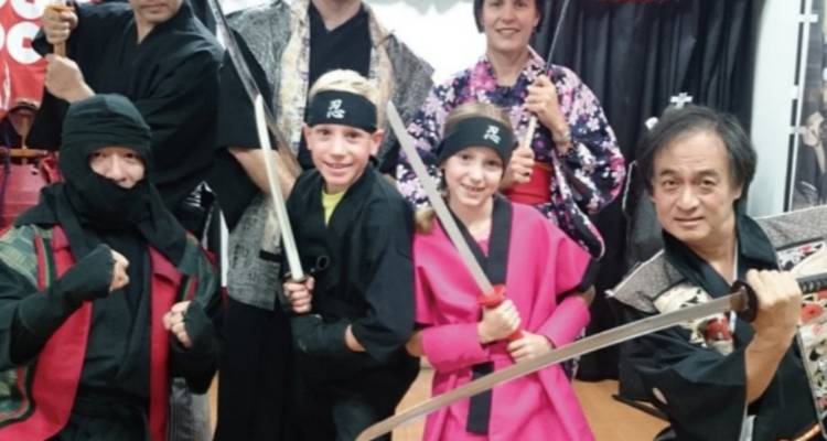 Groep mensen verkleed als ninja's die poseren met zwaarden.