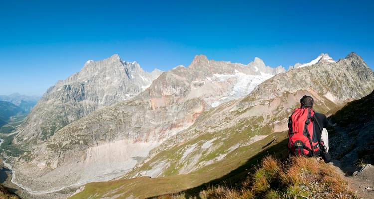 Persona con mochila roja viendo paisaje montañoso.