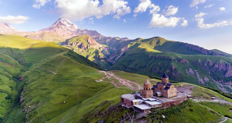 Un paisaje pintoresco con una iglesia en una colina y una montaña nevada al fondo.