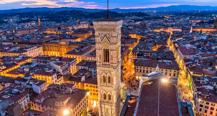 Vue aérienne crépusculaire de Florence avec le Campanile de Giotto dominant les rues illuminées de la ville.