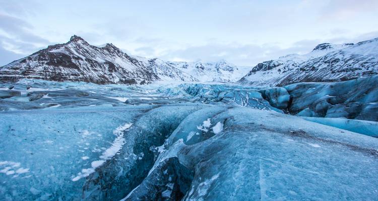 Ausgedehnte blaue Gletscherzungen und schneebedeckte Gipfel im Skaftafell-Nationalpark unter einem blassen Himmel.