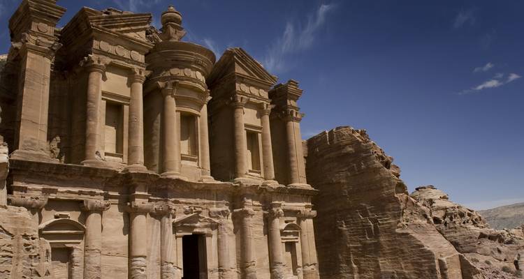 The monumental façade of the Monastery at Petra carved into rose-red rock under a cloudless sky.