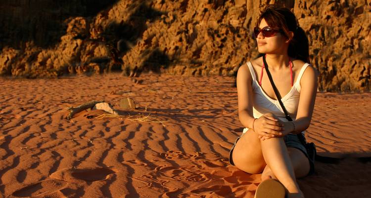 Mujer joven se relaja sobre arena roja brillante al atardecer en el desierto de Wadi Rum