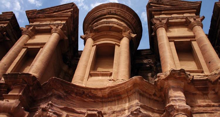 Vue en contre-plongée du Monastère de Pétra sculpté dans les falaises de grès rouge-rose contre un ciel bleu.