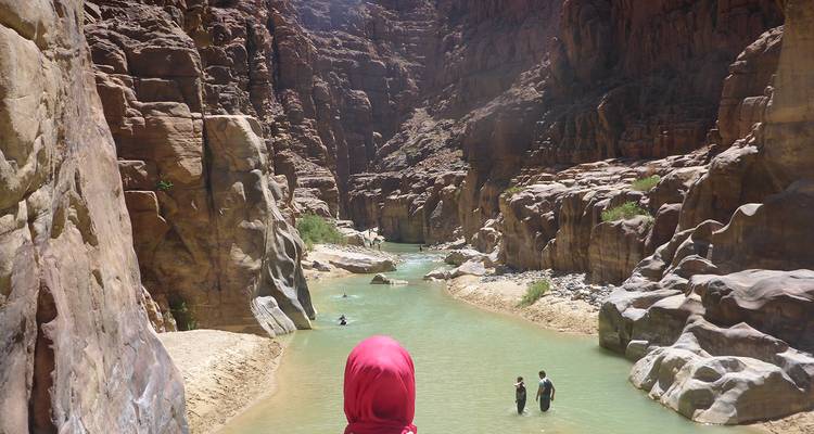 Des voyageurs pataugent dans l'eau émeraude du canyon de Wadi Mujib encadré par d'imposantes parois de grès.