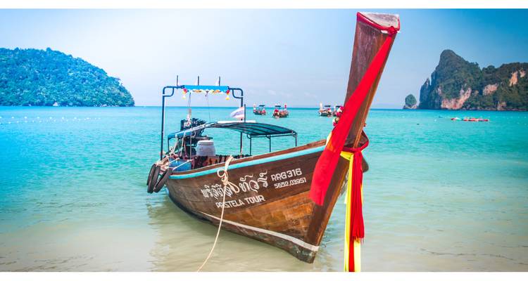 Bateau à longue queue thaïlandais traditionnel amarré sur une eau turquoise cristalline avec des îles en arrière-plan.