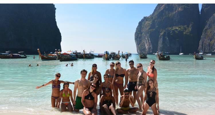 Un grand groupe d'amis posant sur une plage tropicale avec des falaises calcaires et des bateaux à longue queue en arrière-plan.