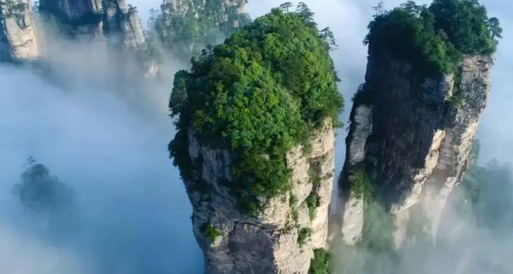 Hohe Steinsäulen mit Grün bewachsen inmitten von Wolken