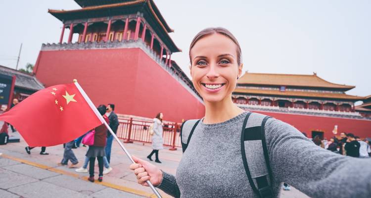 Lächelnde Person mit einer Flagge vor einem traditionellen roten Gebäude im Hintergrund